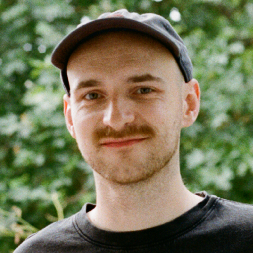 A portrait of Conor Foran smiling at the camera and wearing a cap.